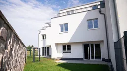 Moderne weiße Reihenhäuser mit kleinen privaten Gärten und einer Steinmauer im Vordergrund.