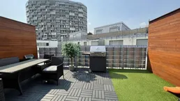 Geräumige Dachterrasse mit Essbereich, Grill und Blick auf moderne Stadtarchitektur.