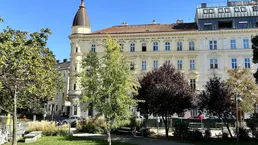 Historisches Gebäude mit markanter Kuppel und einem grünen Park im Vordergrund unter blauem Himmel.