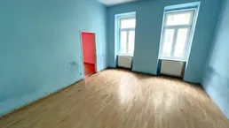 Geräumiger Raum mit hellblauen Wänden, Holzfußboden und zwei Fenstern, bereit zur Renovierung.