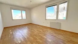 Helles Zimmer mit Parkettboden und zwei Fenstern, bereit zur individuellen Gestaltung.