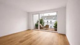 Heller Wohnraum mit neuem Parkettboden und Zugang zu einem kleinen Balkon.