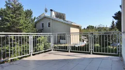 Geräumige Terrasse mit Fliesenboden und Blick auf das Nachbarhaus und viel Grün.