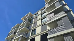 Moderne Wohngebäude-Fassade mit zahlreichen Balkonen und großen Fenstern unter blauem Himmel.