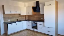 Moderne Einbauküche mit weißen Fronten, Holzoptik-Rückwand und integrierten Geräten.