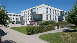 Moderne Wohnanlage mit weißer Fassade, Glasbalkonen und gepflegten Grünflächen unter blauem Himmel.