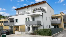 Modernes Mehrfamilienhaus mit weißer und gelber Fassade sowie mehreren Balkonen und Dachterrasse.