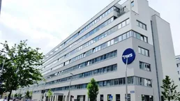 Modernes Bürogebäude mit vielen Fenstern und einer klaren, zeitgenössischen Architektur unter hellem Himmel.