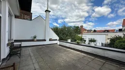 Große gepflasterte Terrasse mit Sitzgelegenheiten und Blick auf den Himmel und umliegende Gebäude.