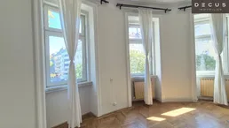 Helles Zimmer mit Fischgrätparkett und hohen Fenstern, die viel Tageslicht hereinlassen.