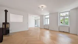 Geräumiges Wohnzimmer mit elegantem Fischgrätparkett, Kaminofen und großen Fenstern.