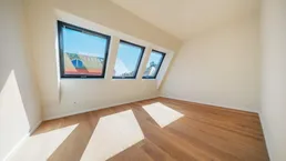 Helles Zimmer im Dachgeschoss mit schrägen Wänden, Dachfenstern und Holzboden.
