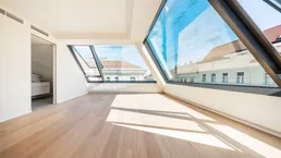 Helles Zimmer mit Holzboden und großen Dachfenstern, die viel Tageslicht hereinlassen.