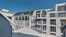 Geräumige Dachterrasse mit Blick auf moderne Gebäude und Solarpaneele unter blauem Himmel.