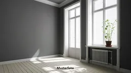 Heller, leerer Raum mit grauen Wänden, Holzboden und großen Fenstern, die viel Tageslicht hereinlassen.