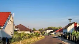 Wohnstraße mit modernen Einfamilienhäusern unter klarem blauen Himmel und gepflegten Grünflächen.