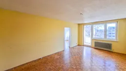 Helles Wohnzimmer mit Fischgrätparkett, gelben Wänden und Zugang zum Balkon.