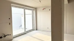 Unfertiger Innenraum mit großen Fenstern und viel Tageslicht während der Bauphase.