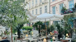 Gemütlicher Außenbereich eines Restaurants mit Tischen, Stühlen und Sonnenschirmen in einer belebten Straße.