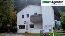 Gebäudeansicht des Gasthofs Haslach mit ImmoAgentur Logo und umgebender Natur.