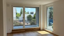 Heller Wohnraum mit Holzboden, großen Fenstern und Zugang zu einem Balkon oder einer Terrasse.