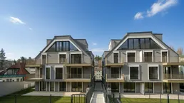 Zwei moderne Mehrfamilienhäuser mit Balkonen, großen Fenstern und gepflegten Grünflächen unter blauem Himmel.