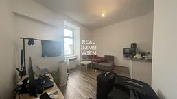 Heller Wohnbereich mit integrierter Küchenzeile, Sofa und Arbeitsplatz.