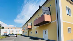 Gelbe Fassade eines modernen Wohngebäudes mit Balkonen und Parkplätzen unter blauem Himmel.