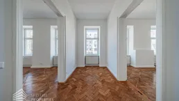 Heller Innenraum mit Fischgrätparkett und hohen Türen, der mehrere Zimmer verbindet.