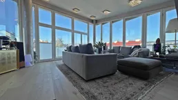 Helles Wohnzimmer mit großen Fenstern, die viel Tageslicht hereinlassen und einen weiten Blick bieten.