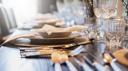 Ein elegant gedeckter Esstisch mit glänzendem Besteck und Kristallgläsern, bereit für eine festliche Mahlzeit.