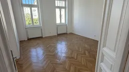 Helles, leeres Zimmer mit Fischgrätparkettboden und zwei Fenstern, bereit zur individuellen Gestaltung.