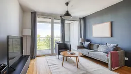 Modernes Wohnzimmer mit Holzboden, bequemer Couch und Zugang zum Balkon.