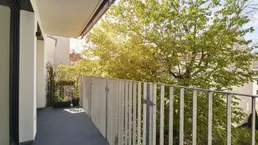 Heller Balkon mit Holzboden und Blick ins Grüne, ideal für entspannte Stunden im Freien.