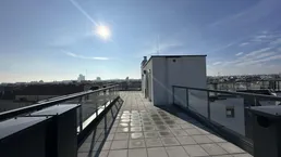 Sonnige Dachterrasse mit Fliesenboden, Glasgeländer und weitem Blick über die Stadt.