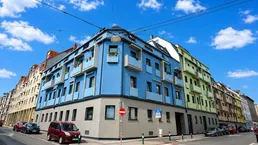 Modernes Eckgebäude mit blauer und grüner Fassade, Balkonen und Blick auf die Stadtstraße.