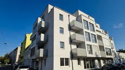 Modernes Mehrfamilienhaus mit Balkonen und großen Fenstern unter blauem Himmel.