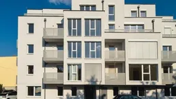 Moderne Wohnhausfassade in Weiß mit großen Fenstern und Balkonen unter blauem Himmel.
