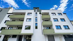 Moderne Wohnhausfassade mit weißen Wänden und grünen Balkonen unter blauem Himmel.
