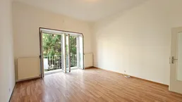 Helles Zimmer mit Parkettboden, weißen Wänden und Zugang zu einem kleinen Balkon.