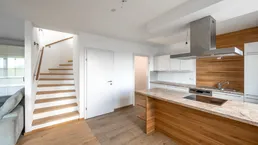 Moderne Küche mit Kochinsel, Granitarbeitsplatte und Holztreppe zum oberen Stockwerk.