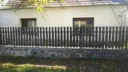 Altes Haus mit Holzzaun und Ziegeldach, umgeben von Herbstlaub und einem Hausnummernschild.