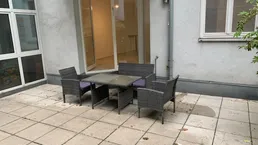 Gepflasterte Terrasse mit Outdoor-Sitzmöbeln und direktem Zugang zu einem hellen Innenraum.