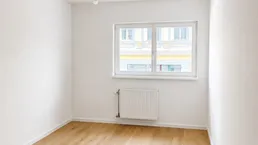 Heller, leerer Raum mit Parkettboden und einem Fenster, das Tageslicht hereinlässt.