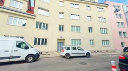 Fassade eines Mehrfamilienhauses mit mehreren Fenstern und Eingangsbereich an einer städtischen Straße.