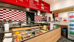Innenansicht eines Schnellrestaurants mit Theke, Zubereitungsbereich und Getränkekühlschrank.
