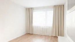 Helles, leeres Zimmer mit Laminatboden und großen Fenstern, bereit zur individuellen Gestaltung.