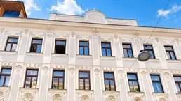 Historische Fassade eines Altbaus mit vielen Fenstern unter strahlend blauem Himmel.