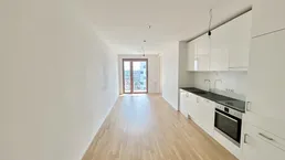 Heller, offener Wohnbereich mit integrierter Küchenzeile, Parkettboden und Zugang zum Balkon.