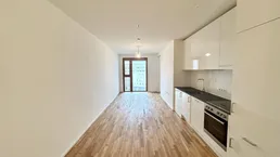 Heller, offener Wohnbereich mit integrierter Küchenzeile, Parkettboden und Zugang zum Balkon.